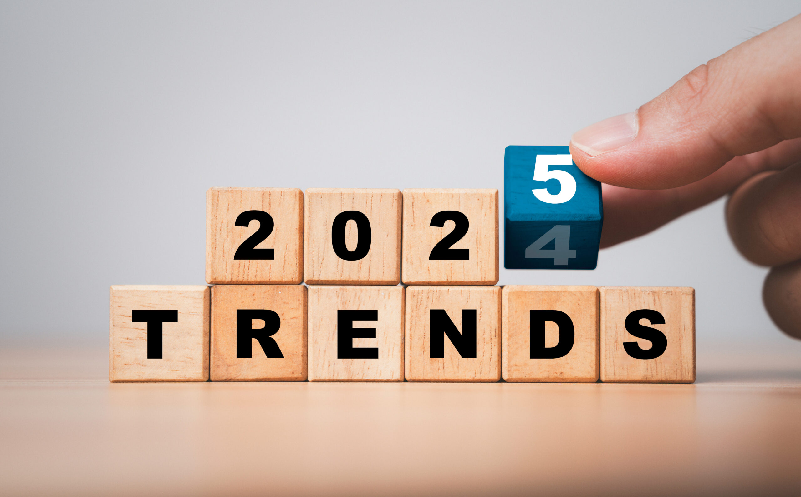 Wooden blocks spelling "2024 TRENDS," with a hand flipping the "4" to "5" on a blue block.