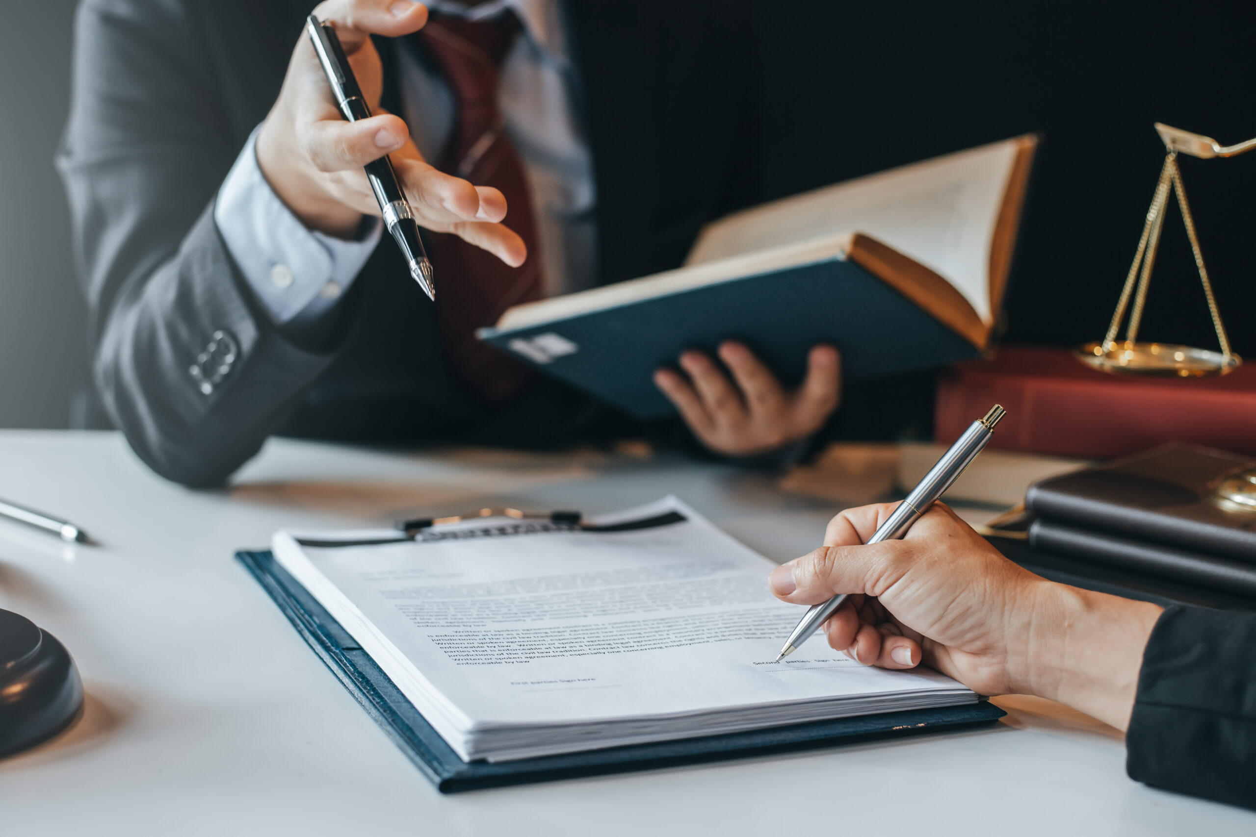 A professional consultation with a client signing a contract, legal scales and documents visible on the table.